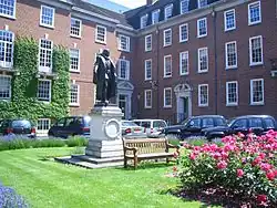 A grassy area with floral shrubs and a central statue on a plinth, with terraced buildings in the background