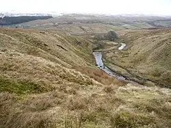 A small stream meandering through a narrow valley with snow-covered hills in the distance
