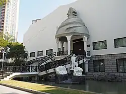 The entrance of a building, accessed through curved staircases; in front of the building are three statues, representing Gao Jianfu, Chen Shuren, and Gao Qifeng