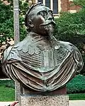 A copper bust of King Gustav Adolph's shoulders and head. He wears his military garb and a crown of laurels. His eyes are fixed at a point in the sky and his chin tilts upward confidently. He wears a full mustache and a triangular goatee. The bust is from Gustavus Adolphus College in Minnesota.