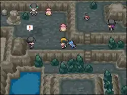 A pre-teenaged boy with black hair and a black and yellow baseball cap stands inside a dark, rocky, cave-like area. A small, blue, crocodile-like Pokémon stands behind him. Standing elsewhere in the area are two young men and one young woman, all wearing black clothes and beanies, and two small, pink, quadrupedal Pokémon.