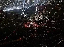 A faraway dark-lit image with minuscule lights going in straight line from the center where a stage can be seen.