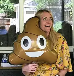 A woman smiling and holding a brown balloon with a large, smiling face. It is a triangle with swirly sides.