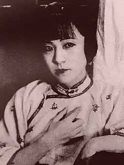 A monochrome image of a woman in a high-collared shirt holding her hand to her chest