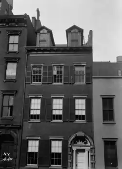 A black-and-white image of the Merchant's House Museum's exterior as seen in 1936. The house is four stories high and has a brick facade. There are buildings on either side.