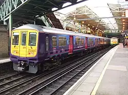 A commuter train at a station. Below the train, four rails are visible—two are for the wheels and one provides power. Above the train, a catenary power line is also visible.