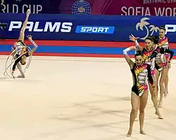 One gymnast stands in a back split with several hoops while four others perform