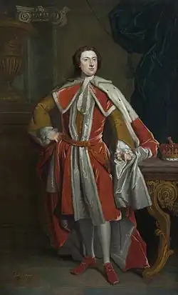 A man in courtly dress is shown standing, wearing ermine robes over a mustard-coloured jacket
