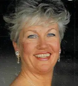 Publicity shot of Kari Løvaas. She was then a middle-aged, white woman with blue eyes, short, curly grey hair, dangling earrings, red lipstick and blue eyeshadow.