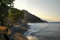 View parallel to a small, gravelly beach on the ocean, with a hill in the background