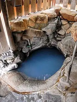 An image of a hot spring bath carved out of rock in a wooden building.