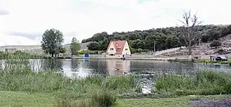 A small house by a body of water surrounded by grass and trees.