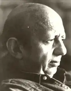 Profile black and white publicity shot of an unsmiling, clean-shaven man with receding hair, and a straight nose.