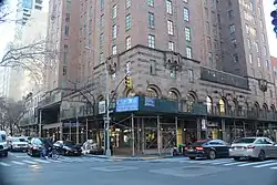 The Barbizon's ground-level facade as seen from the intersection of 63rd Street and Lexington Avenue. There are large archways with storefronts. On the right, there is scaffolding in front of the storefronts.