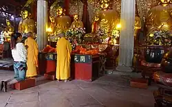 Monks and a lay follower in front of statues of the Five Tathagathas at the Mahavira Hall of Kaiyuan Temple in Quanzhou, Fujian, China