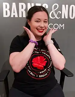 A white woman with brown hair is wearing a black t-shirt (that reads "dark universe"); she is wearing sunglasses, looking and facing the camera's left.