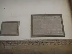 Two plaques on a white wall from a low point of view.