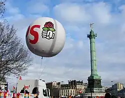 A balloon with the letters "PS" and a schematic right fist holding a rose. In the background, the Vendôme Column of Paris.