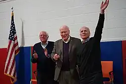 Three older men on a stage next to an American flag.