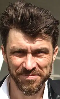close-up of Marcin Czarnik wearing a white shirt and black jacket, squinting and looking directly at camera