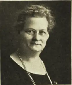 B&W portrait photo of a woman with wavy hair wearing a black, scooped neck blouse, and a beaded necklace