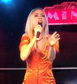 Maria Entraigues in an orange dress singing into a microphone