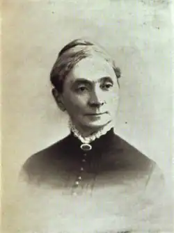 B&W portrait photo of a woman with her hair in an up-do, wearing a dark blouse with white fringe at the collar