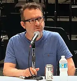 Mark Anthony-Turnage speaks into a microphone during a conference.