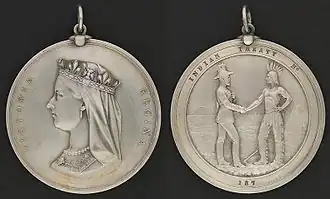 Photograph showing the two sides of a round silver medal, showing the profile of Queen Victoria on one side and the inscription "Victoria Regina", with the other side having a depiction of a man in European garb shaking hands with a man in historical First Nation clothing with the inscription "Indian Treaty 187"