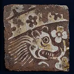 A square floor tile with an image of a lion and a flower.
