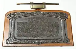 Colour photograph of a bronze memorial tablet on an oak backing