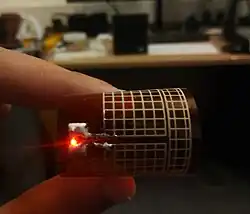 A printed rectenna lighting an LED from a Powercast 915&nbsp;MHz transmitter, flexible meshed antenna bent with a red LED light