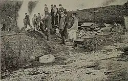 Miners with shovels and wheelbarrows working at an ore heap (c. 1907)