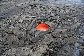 A "skylight" hole, about 6&nbsp;m (20&nbsp;ft) across, in a solidified lava crust reveals molten lava below (flowing towards the top right) in an eruption of Kīlauea in Hawaii