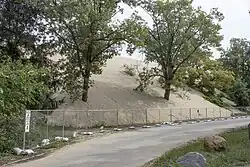 A metal fence is shown in front of a massive dune which is overtaking the road.