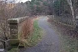 Between the parapet wall on the left and the cast iron railings on the right, a footpath where once there were rails extends across the viaduct, curving gently towards the right and the tunnel mouth