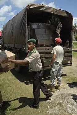 Two young people are seen unloading boxes from the back of a large truck, with one of them handing a box to a person out of frame.