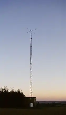 Tall antenna tower on a background of twilight clear sky; small shack is at bottom of tower