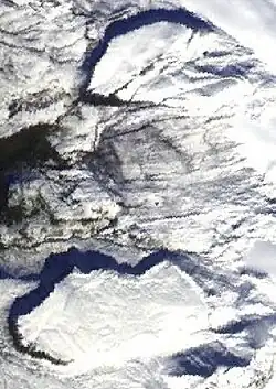 An overhead view of two flat-topped, steep-sided, snow-covered rocky hills on a barren surface.