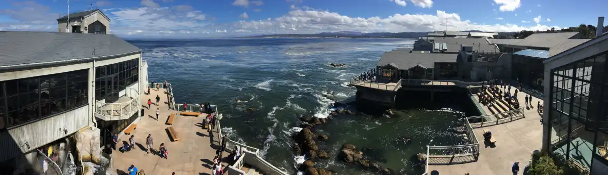 Panoramic view of the aquarium's 20,000 square feet (1,900&nbsp;m2) of public decks overlooking Monterey Bay. The building's walls on either side consist mostly of windows, but there is stadium seating to the right overlooking a man-made tide pool