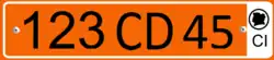 Plate with a single row of black alphanumeric characters on an orange background, and a white bar on the right side containing the black letters CI at the bottom, and a black silhouette of the Ivory Coast inside a black circle at the top.