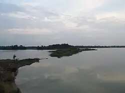 A photo showing the calm water of a quarry lake, with forested areas far in the background and small bits of land from a peninsula visible in the center and at the left edge.