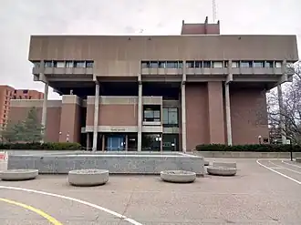 A topheavy concrete and brick building stands before a courtyard and paths.