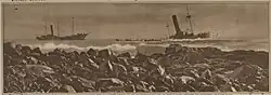 B&W image of a half-sunken ship stranded just off shore
