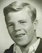 A black and white photograph of a smiling teen boy with braces