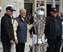 Rick Mears, Al Unser, and A. J. Foyt standing beside the Borg-Warner Trophy in 2021