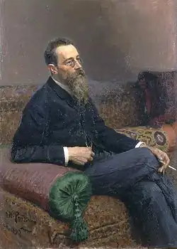 A man with glasses and a long beard sitting on a sofa, smoking