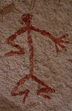 Humanoid stick figure painted on a rock wall in red. The figure is shown in Stylistic group&nbsp;C.