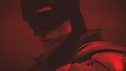 Robert Pattinson in costume as Batman with red hued lighting.