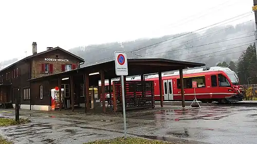 Two-story building with gabled roof next to railway line with red train